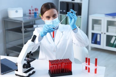 Photo of Laboratory testing. Doctor dripping blood sample into test tube at table indoors