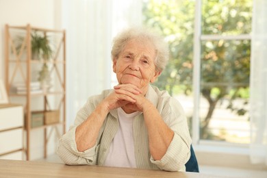 Portrait of beautiful senior woman at wooden table indoors