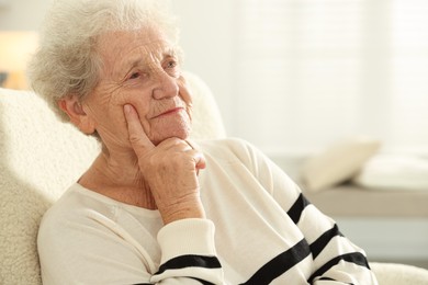 Photo of Pensive senior woman sitting on armchair at home