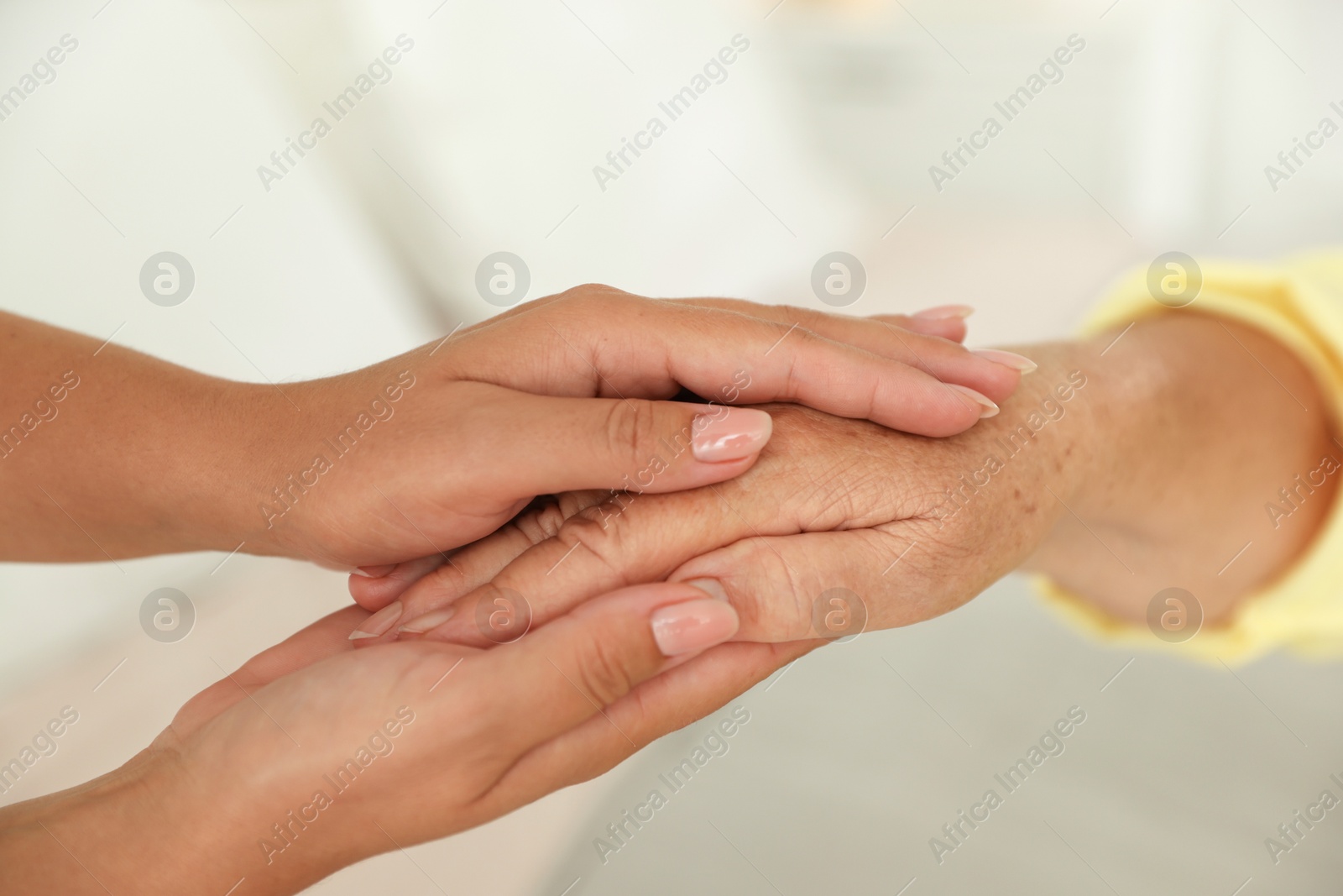 Photo of Young and elderly women holding hands indoors, closeup