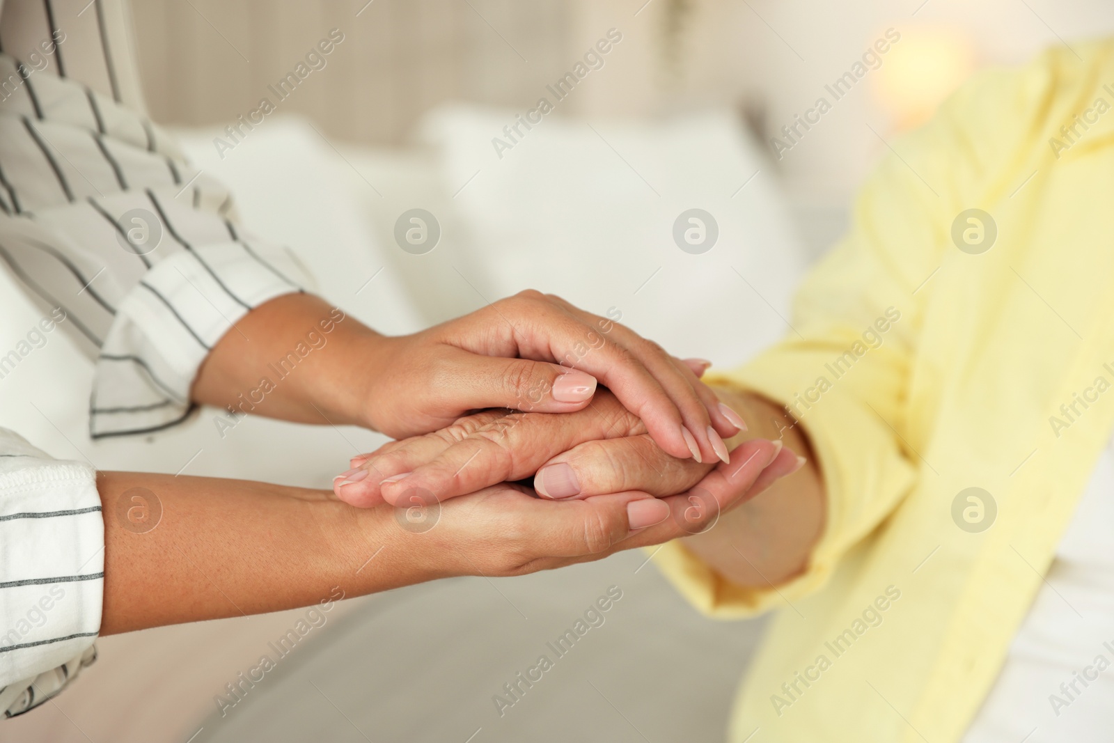 Photo of Young and elderly women holding hands indoors, closeup