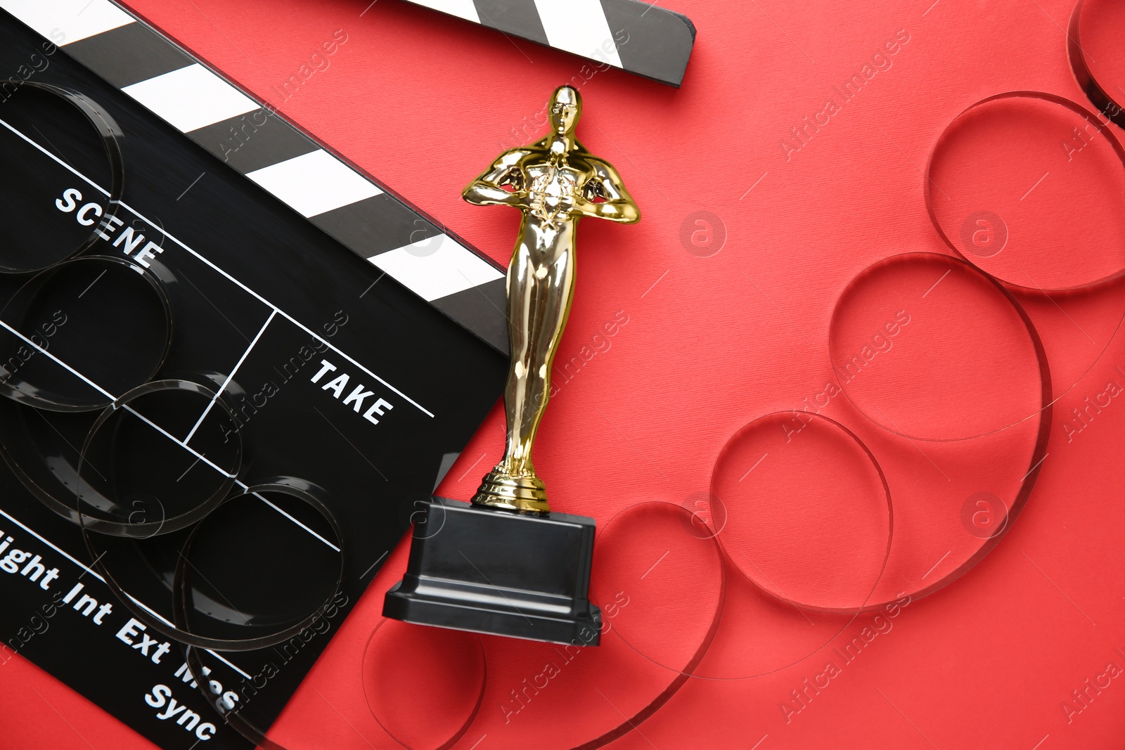 Photo of Golden trophy in shape of human figure, movie clapper and film reel on red background, top view