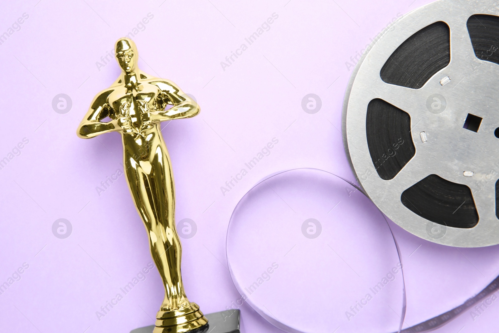 Photo of Golden trophy in shape of human figure and film reel on violet background, top view