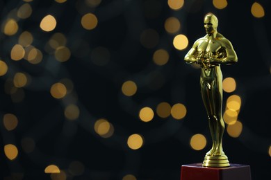 Photo of Golden trophy in shape of human figure on black background with blurred lights, space for text