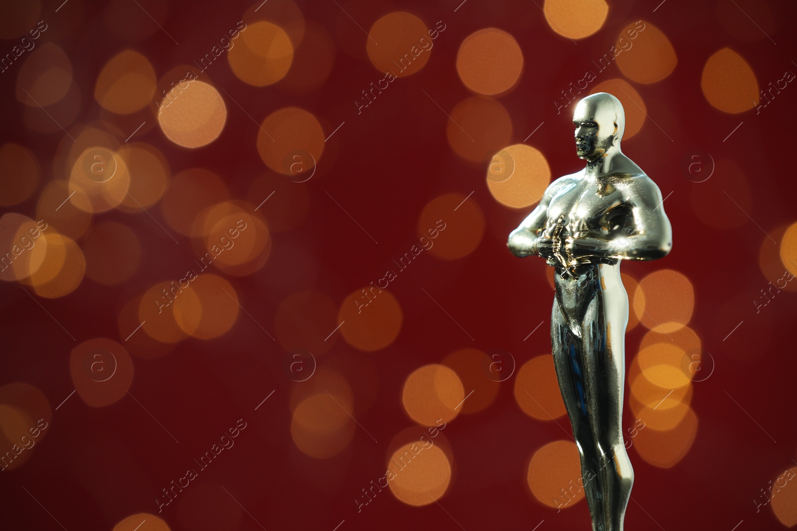 Photo of Golden trophy in shape of human figure on red background with blurred lights, space for text