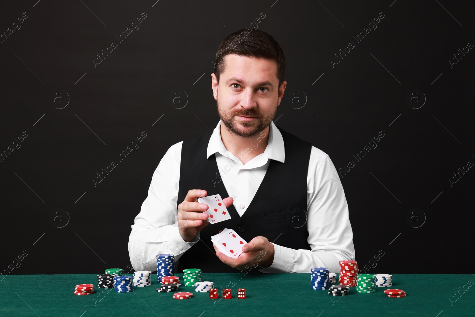 Photo of Professional croupier shuffling cards at gambling table against black background