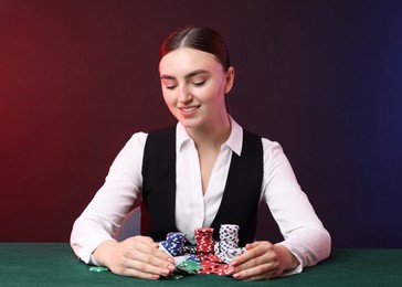 Photo of Professional croupier with casino chips and playing cards at gambling table on color background