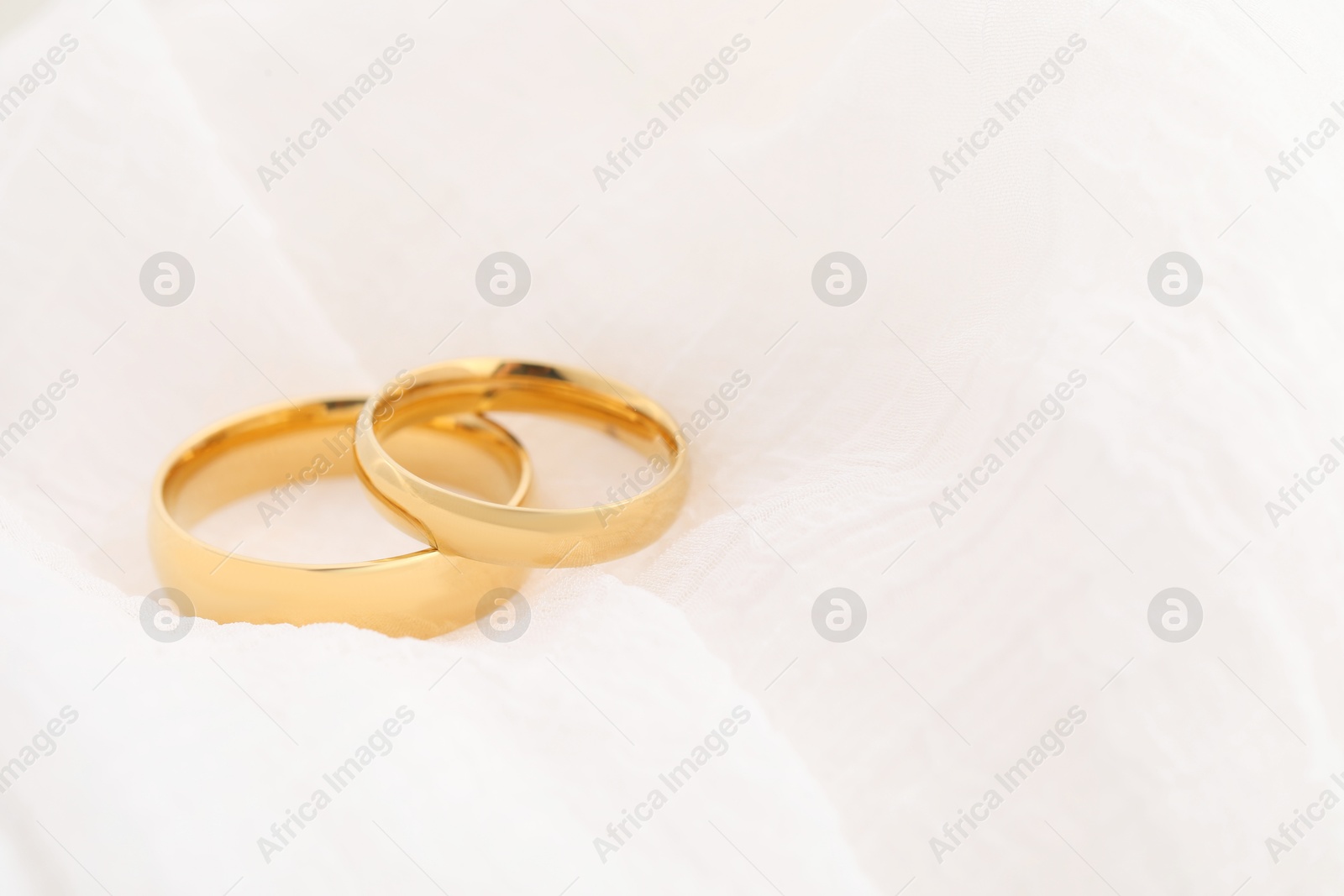 Photo of Beautiful golden wedding rings on white fabric, closeup. Space for text