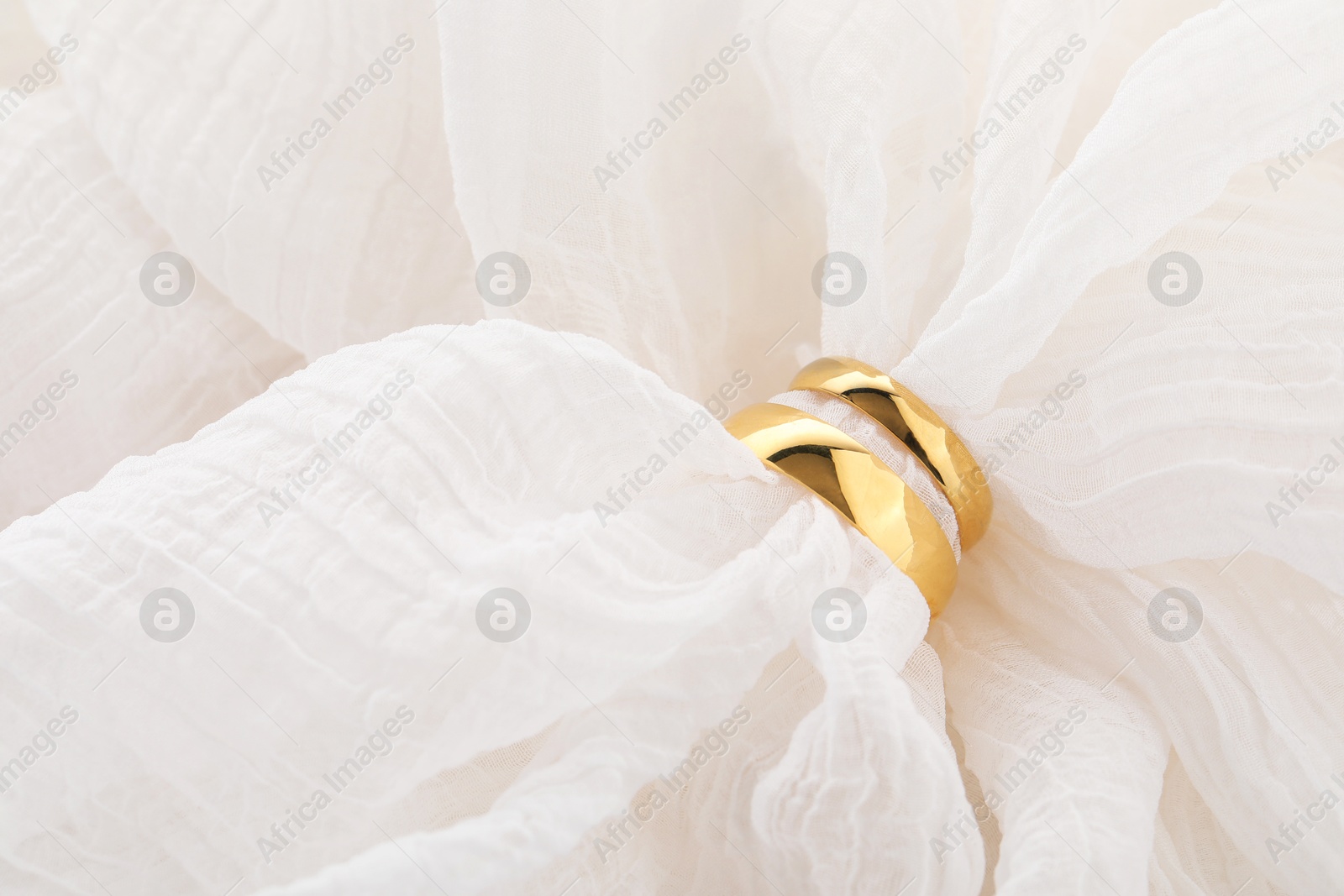 Photo of Beautiful golden wedding ring on white fabric, top view