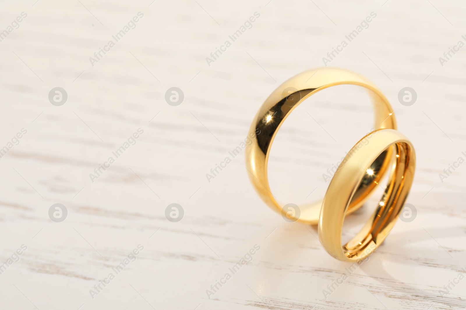 Photo of Beautiful golden wedding rings on light wooden background, space for text