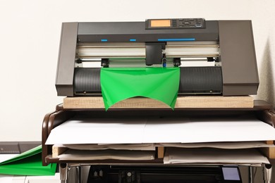 Photo of Modern cutting machine with green vinyl sheet indoors