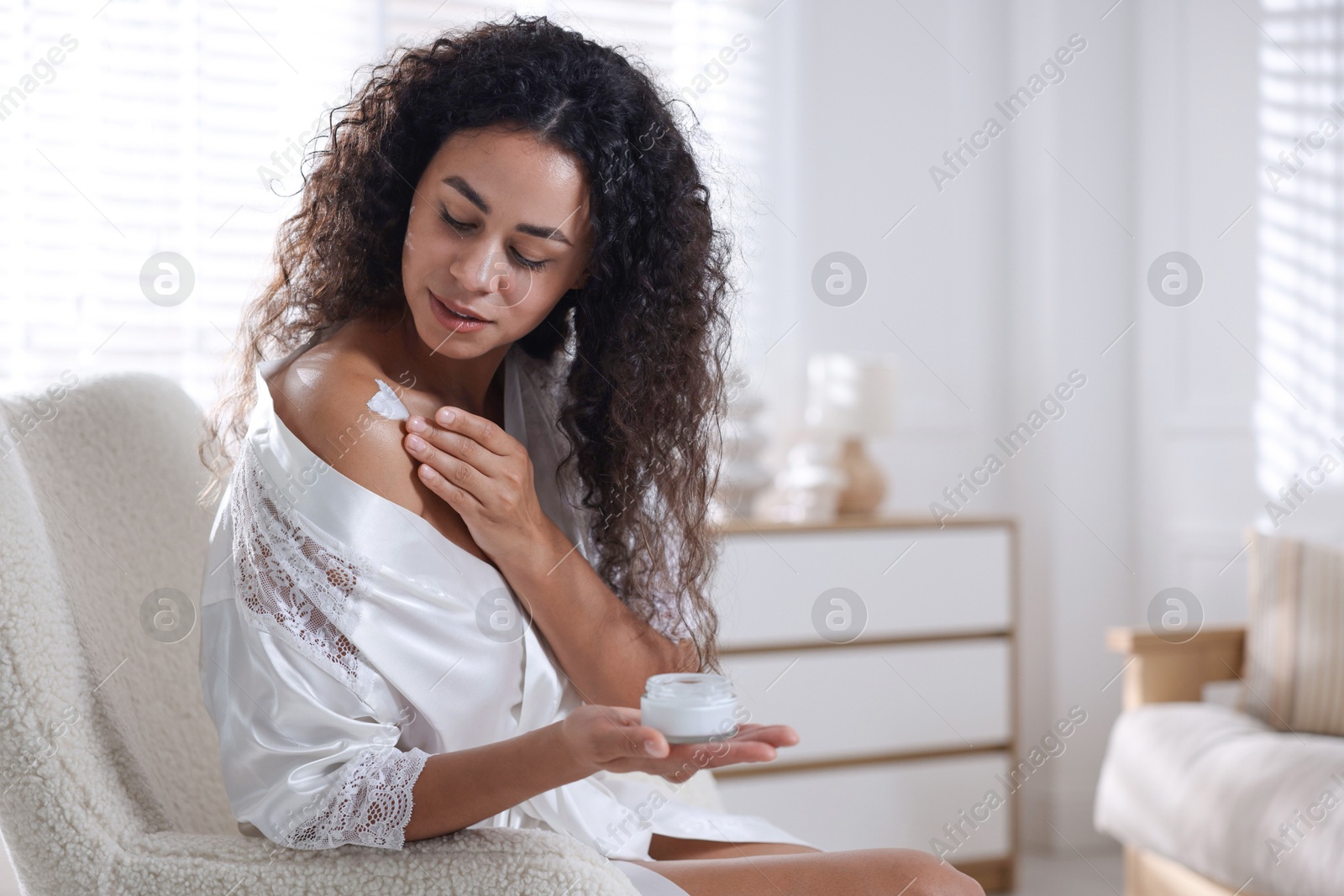 Photo of Young woman applying cream onto shoulder at home. Space for text