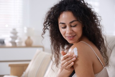 Photo of Young woman applying cream onto shoulder at home. Space for text