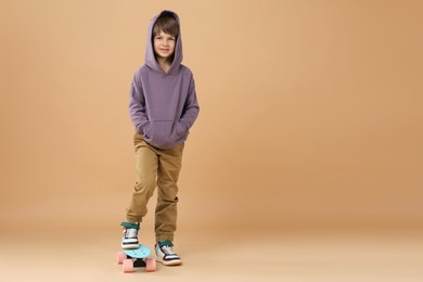 Photo of Little boy with skateboard on beige background, space for text