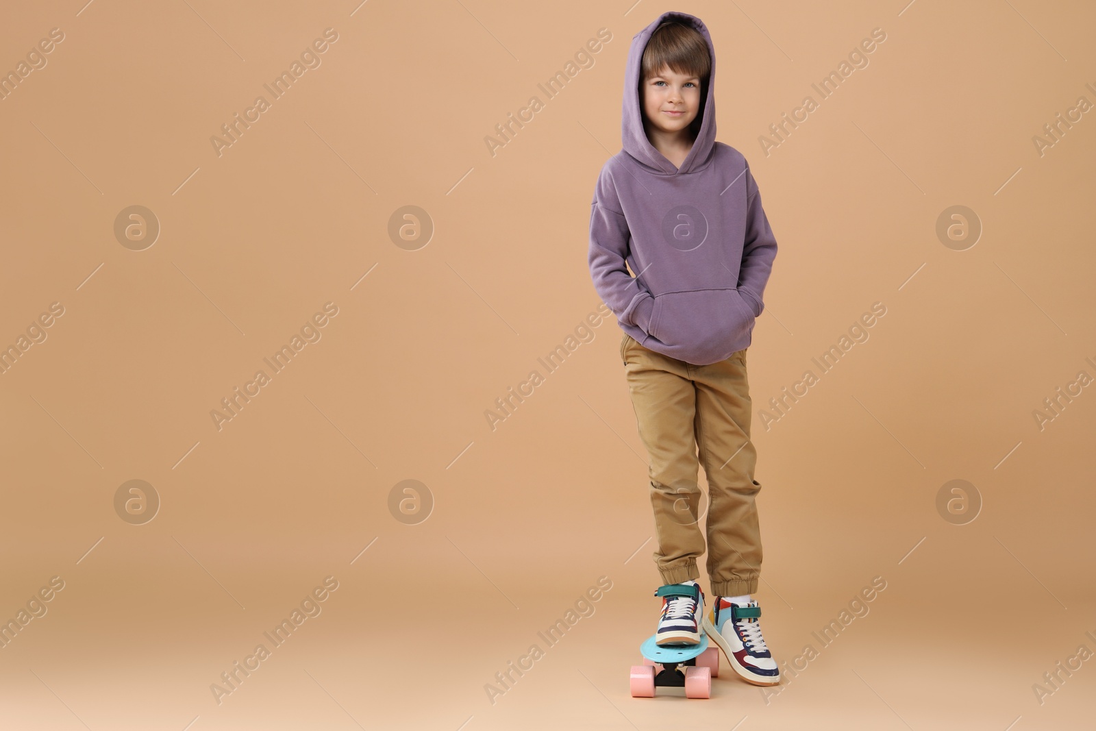 Photo of Little boy with skateboard on beige background, space for text