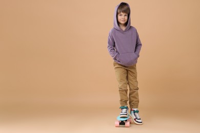 Little boy with skateboard on beige background, space for text