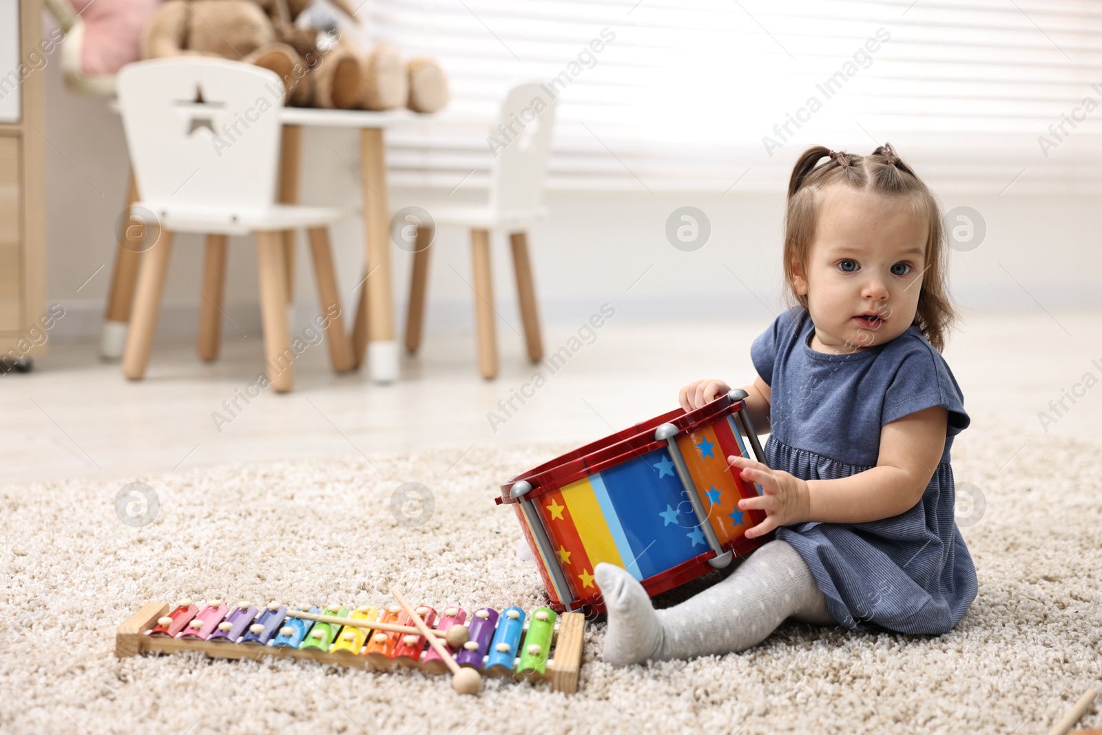 Photo of Cute little girl playing with toy drum on floor at home, space for text