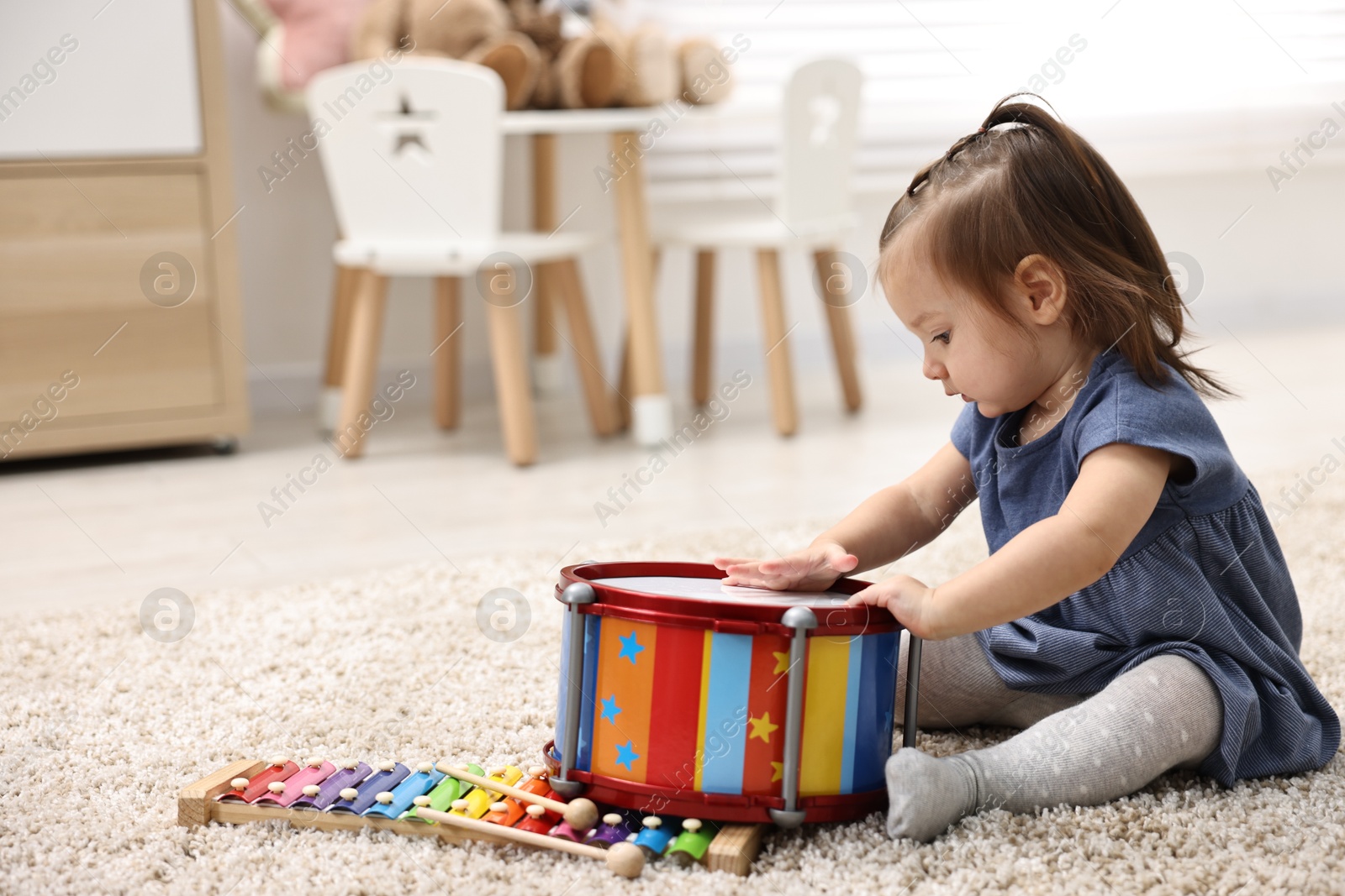 Photo of Cute little girl playing with toy drum on floor at home, space for text