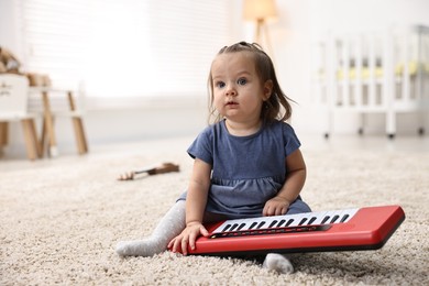 Photo of Cute little girl playing with toy piano at home, space for text