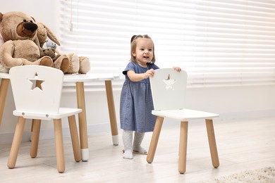 Photo of First steps. Cute little baby with small chair at home