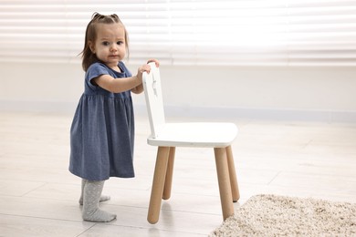 Photo of First steps. Cute little baby with small chair at home