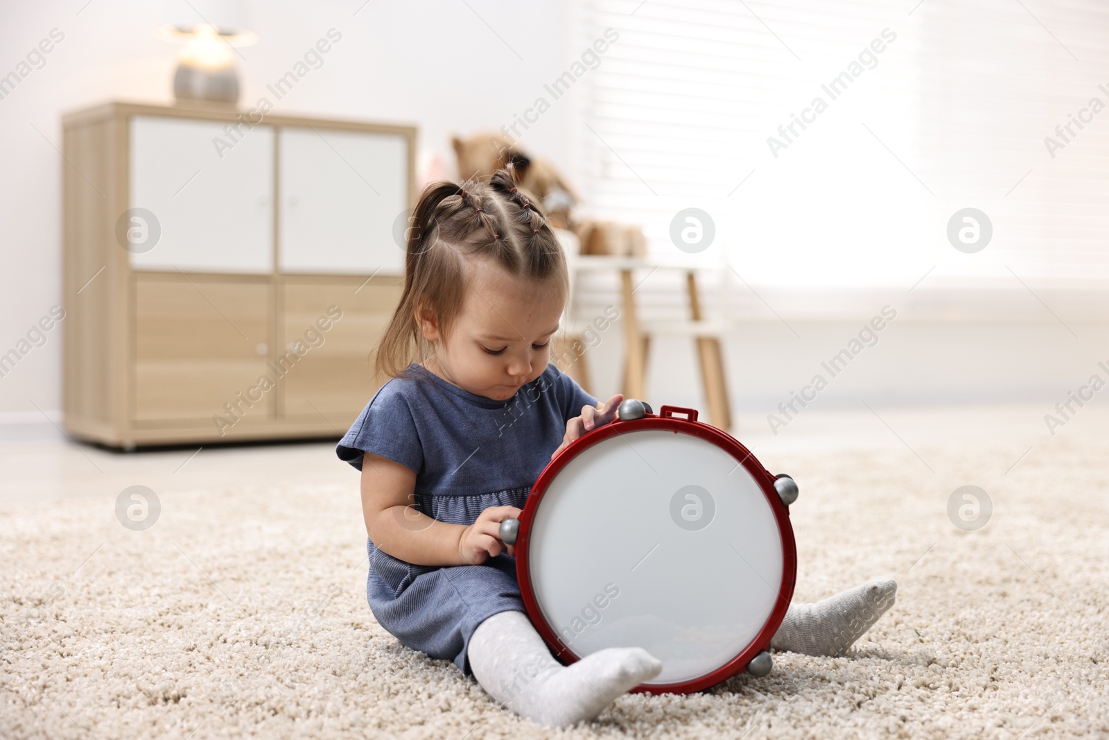 Photo of Cute little girl playing with toy drum on floor at home