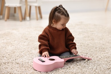 Photo of Cute little girl playing with toy guitar on floor at home