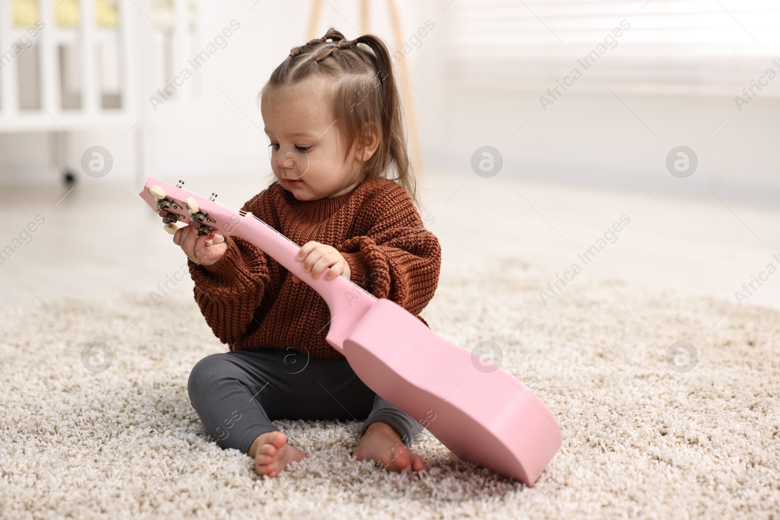 Photo of Cute little girl playing with toy guitar on floor at home