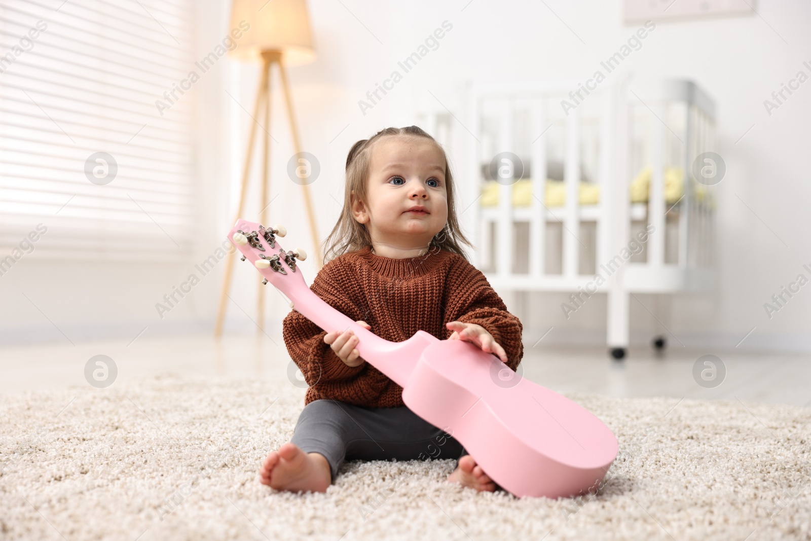 Photo of Cute little girl playing with toy guitar on floor at home