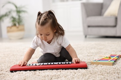 Photo of Cute little girl playing with toy piano at home