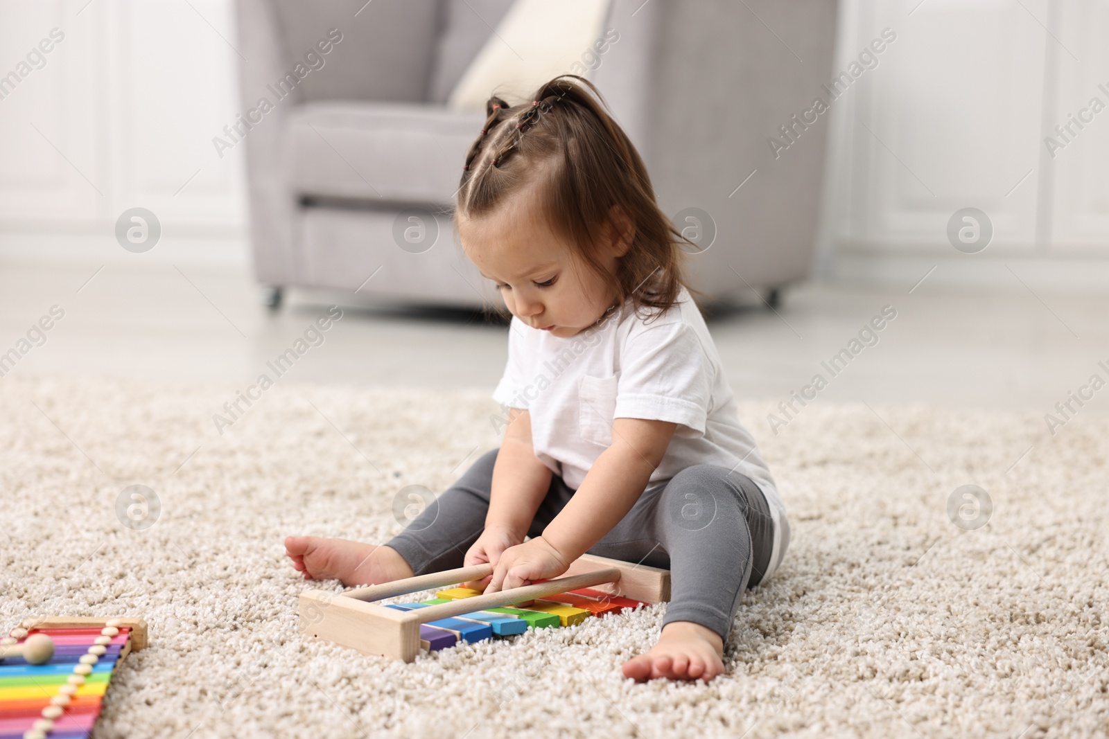 Photo of Cute little girl playing with toy xylophone on floor at home