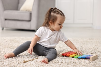 Photo of Cute little girl playing with toy xylophone on floor at home