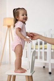 Photo of First steps. Mother supporting daughter while she learning to walk at home, closeup