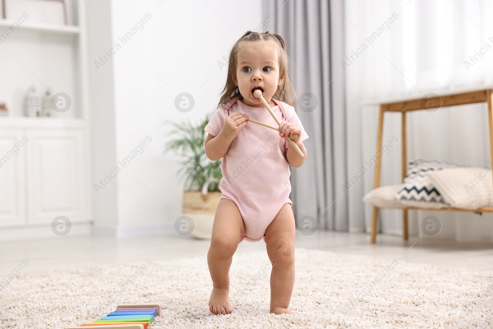 Photo of First steps. Cute little baby with drumsticks learning to walk at home