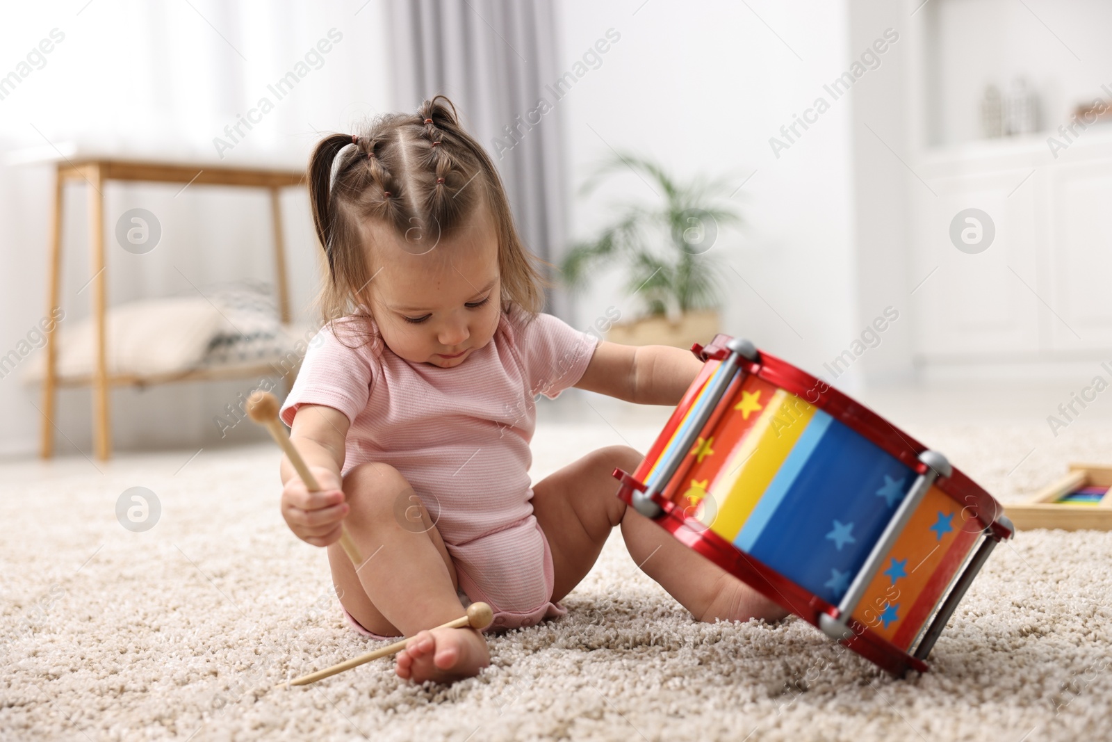 Photo of Cute little girl playing with toy drum and drumsticks on floor at home