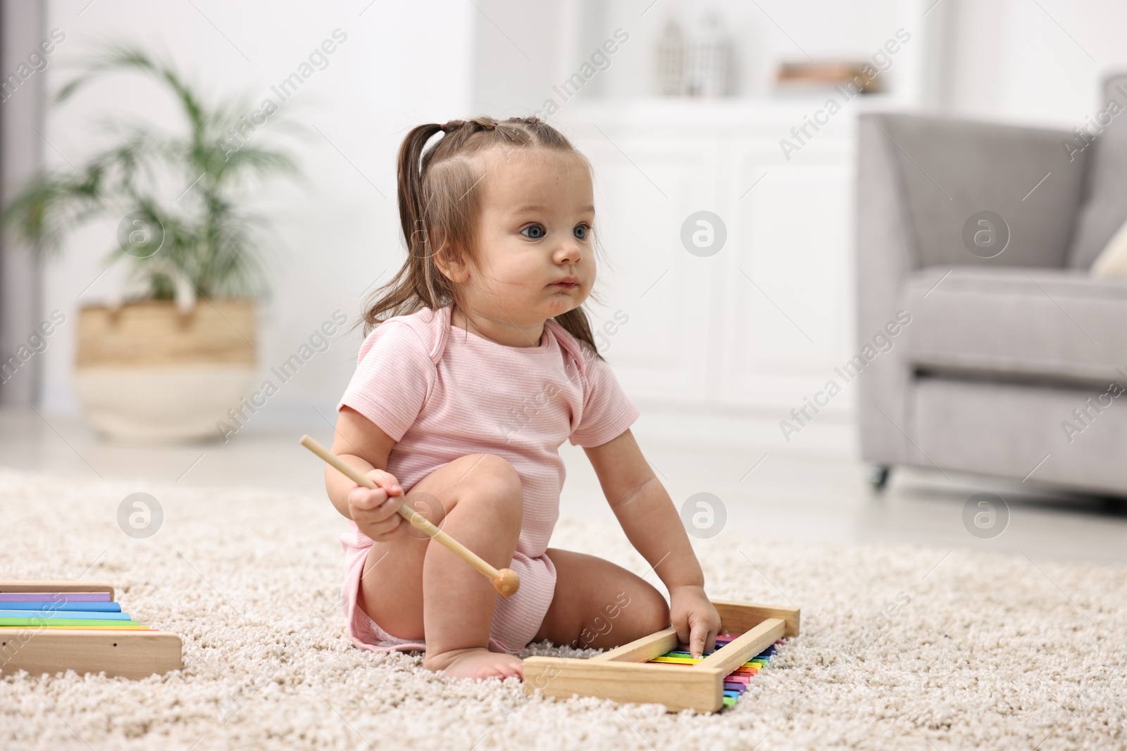 Photo of Cute little girl playing with toy xylophone on floor at home