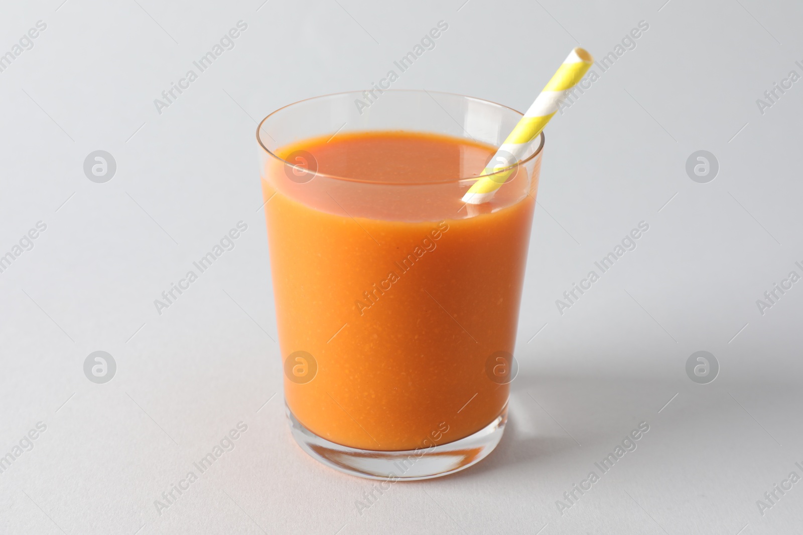 Photo of Fresh carrot smoothie in glass on light grey background, closeup