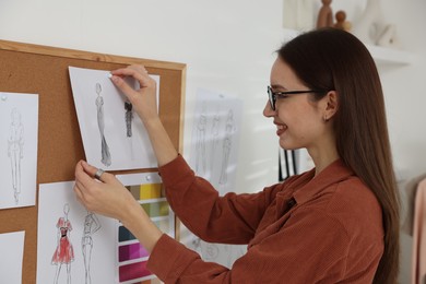 Photo of Fashion designer pinning sketch of clothes to corkboard in workshop