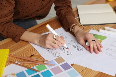 Photo of Fashion designer drawing sketch of clothes at wooden table in workshop, closeup