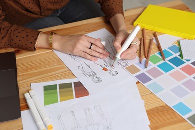 Photo of Fashion designer drawing sketch of clothes at wooden table in workshop, closeup