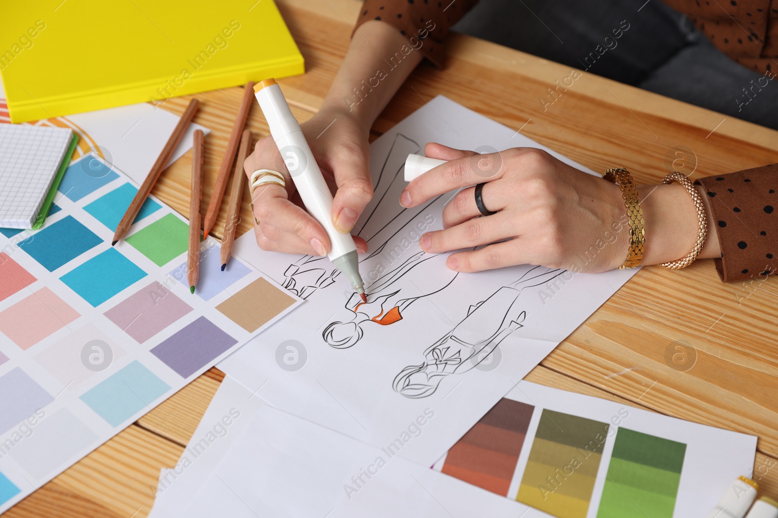 Photo of Fashion designer drawing sketch of clothes at wooden table in workshop, closeup