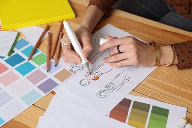 Photo of Fashion designer drawing sketch of clothes at wooden table in workshop, closeup