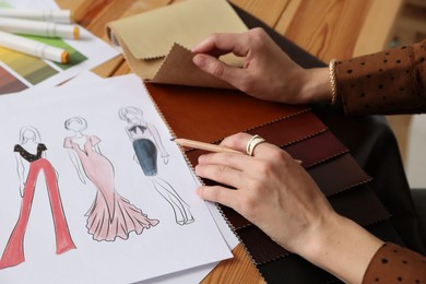 Photo of Fashion designer choosing fabric among colorful samples at wooden table in workshop, closeup