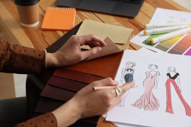 Photo of Fashion designer choosing fabric among colorful samples at wooden table in workshop, closeup