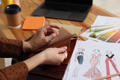 Photo of Fashion designer choosing fabric among colorful samples at wooden table in workshop, closeup