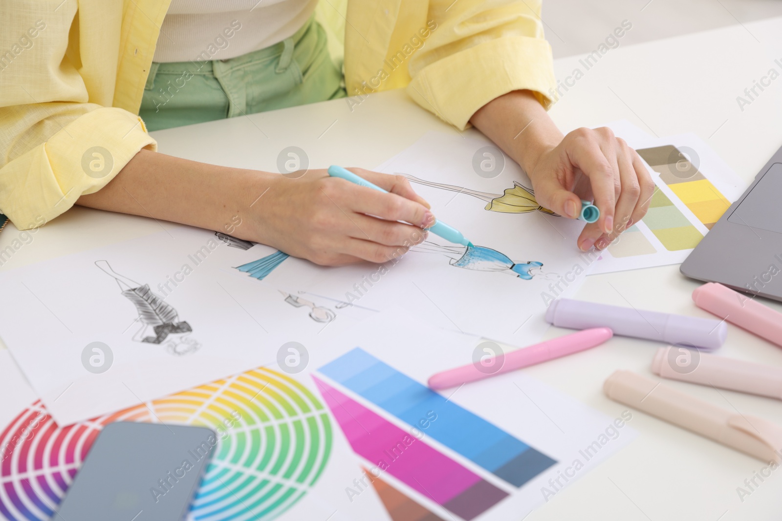 Photo of Fashion designer drawing sketch of clothes at white table in workshop, closeup