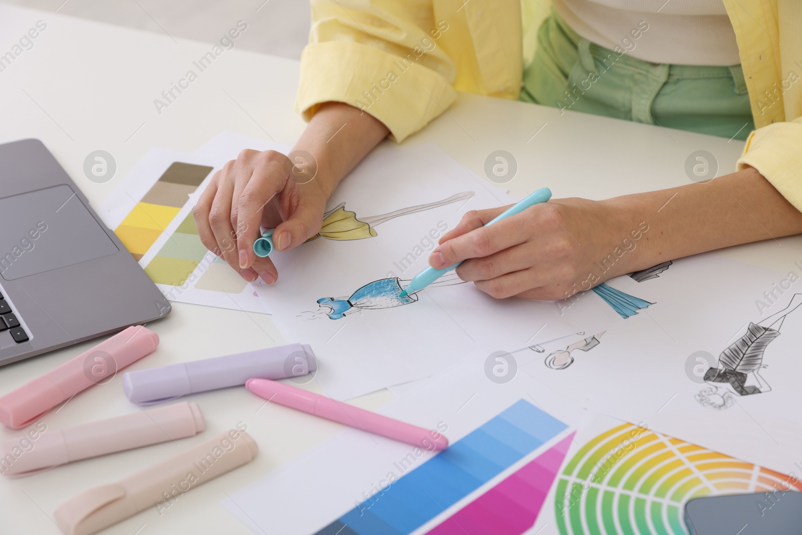 Photo of Fashion designer drawing sketch of clothes at white table in workshop, closeup