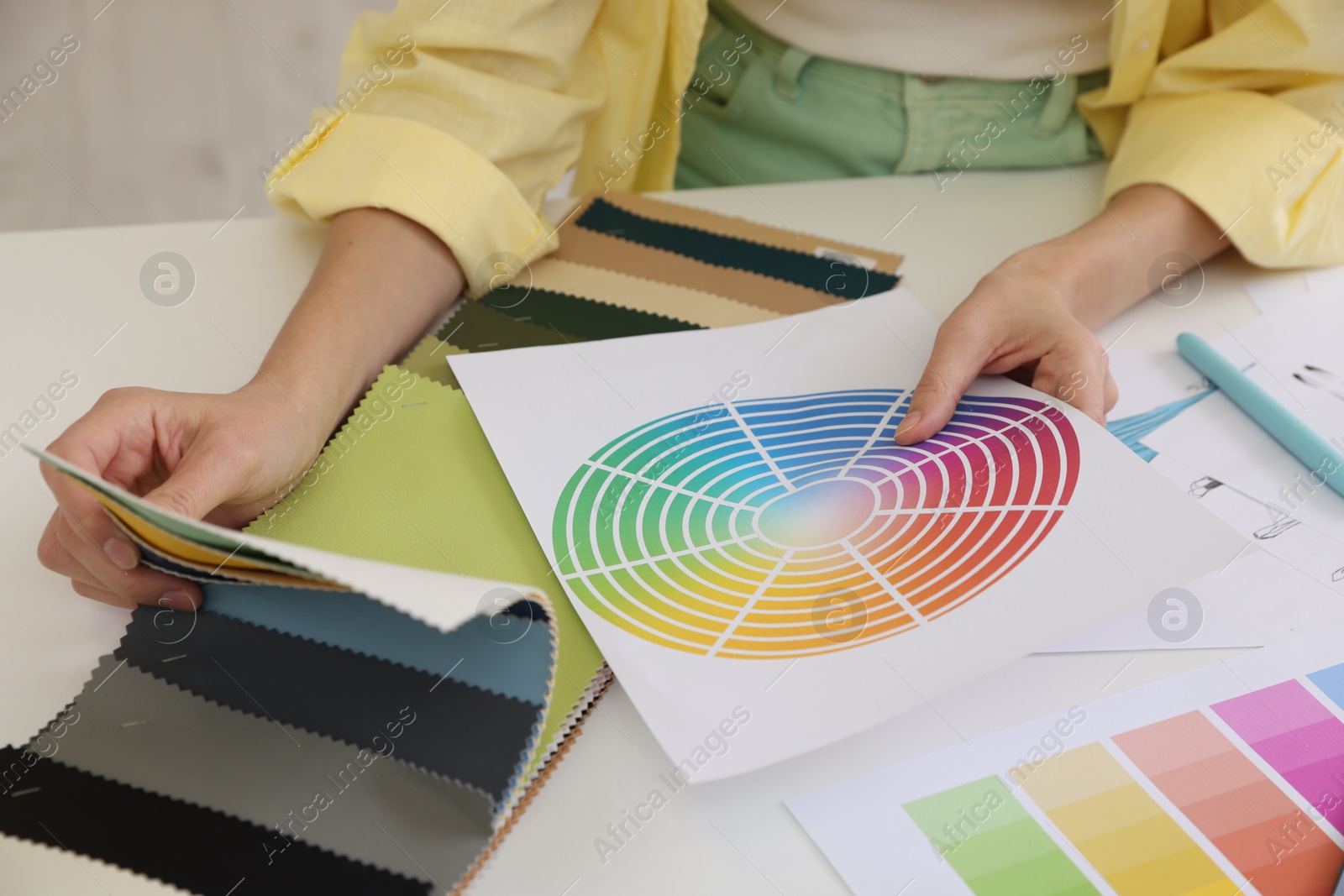 Photo of Fashion designer with color palette choosing fabric among different samples at white table in workshop, closeup