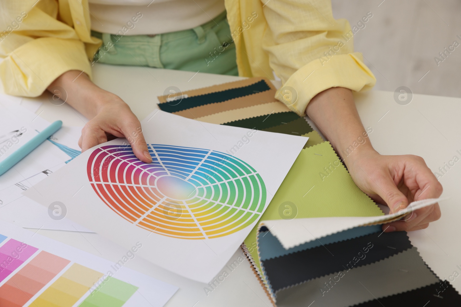 Photo of Fashion designer with color palette choosing fabric among different samples at white table in workshop, closeup