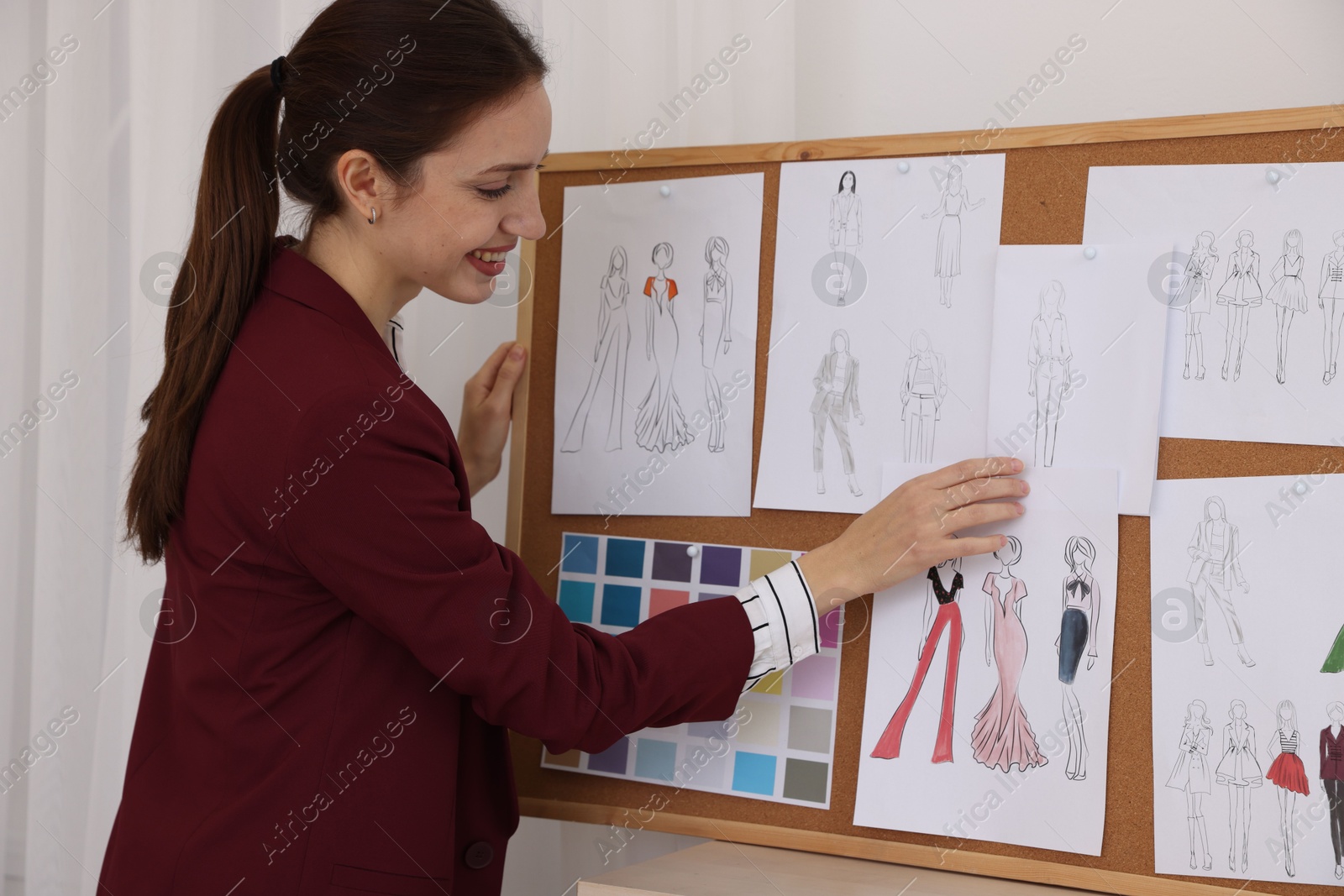 Photo of Fashion designer pinning sketch of clothes to corkboard in workshop